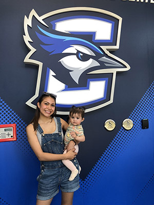 Fatima Salazar holding daughter in front of Creighton Bluejay logo.