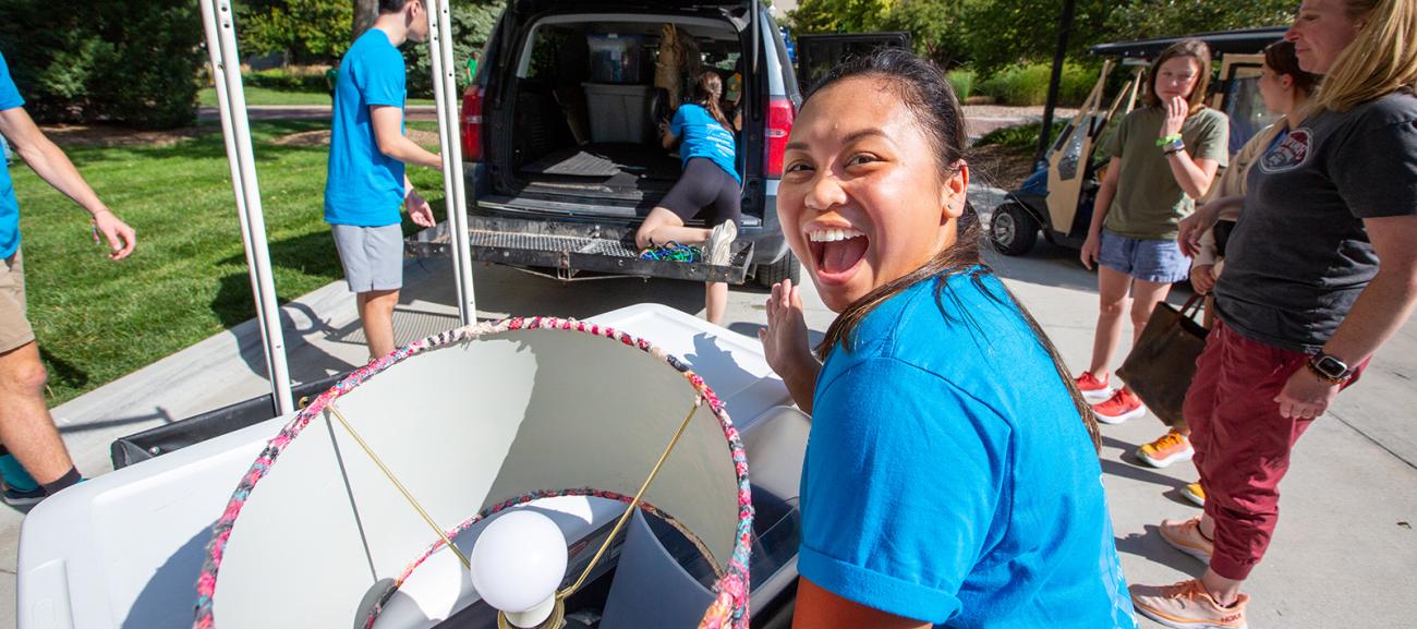 Creighton student smiles for camera while moving a lamp. 