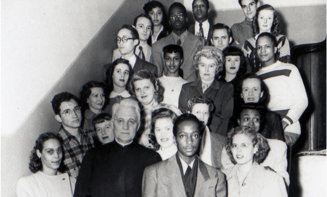 Fr. Markoe (front, second from left) stands by stairs in Creighton Hall with members of the Omaha DePorres Club in the 1940's (black and white photo)