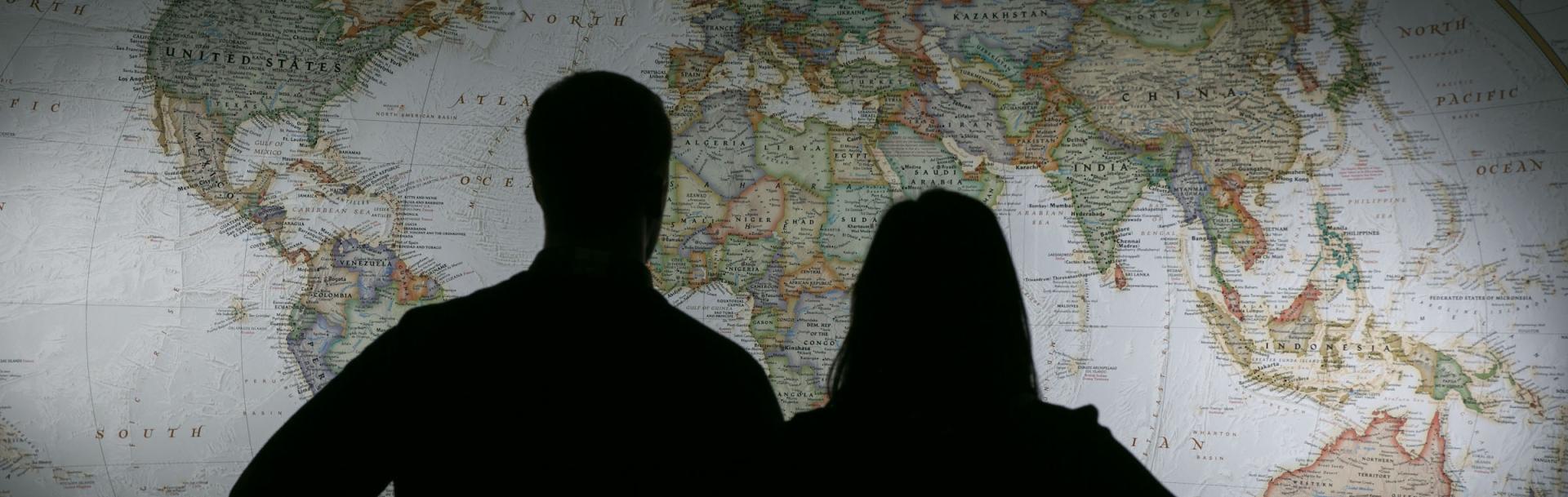 Woman and man silhouetted in front of world map
