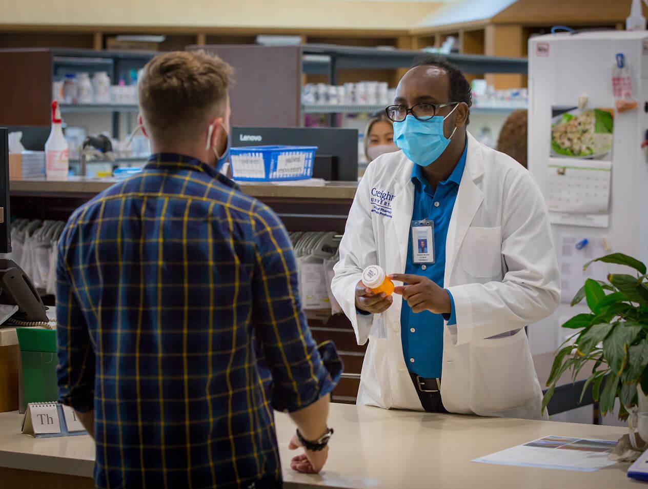 A pharmacy student explains a bottle of medication to a man