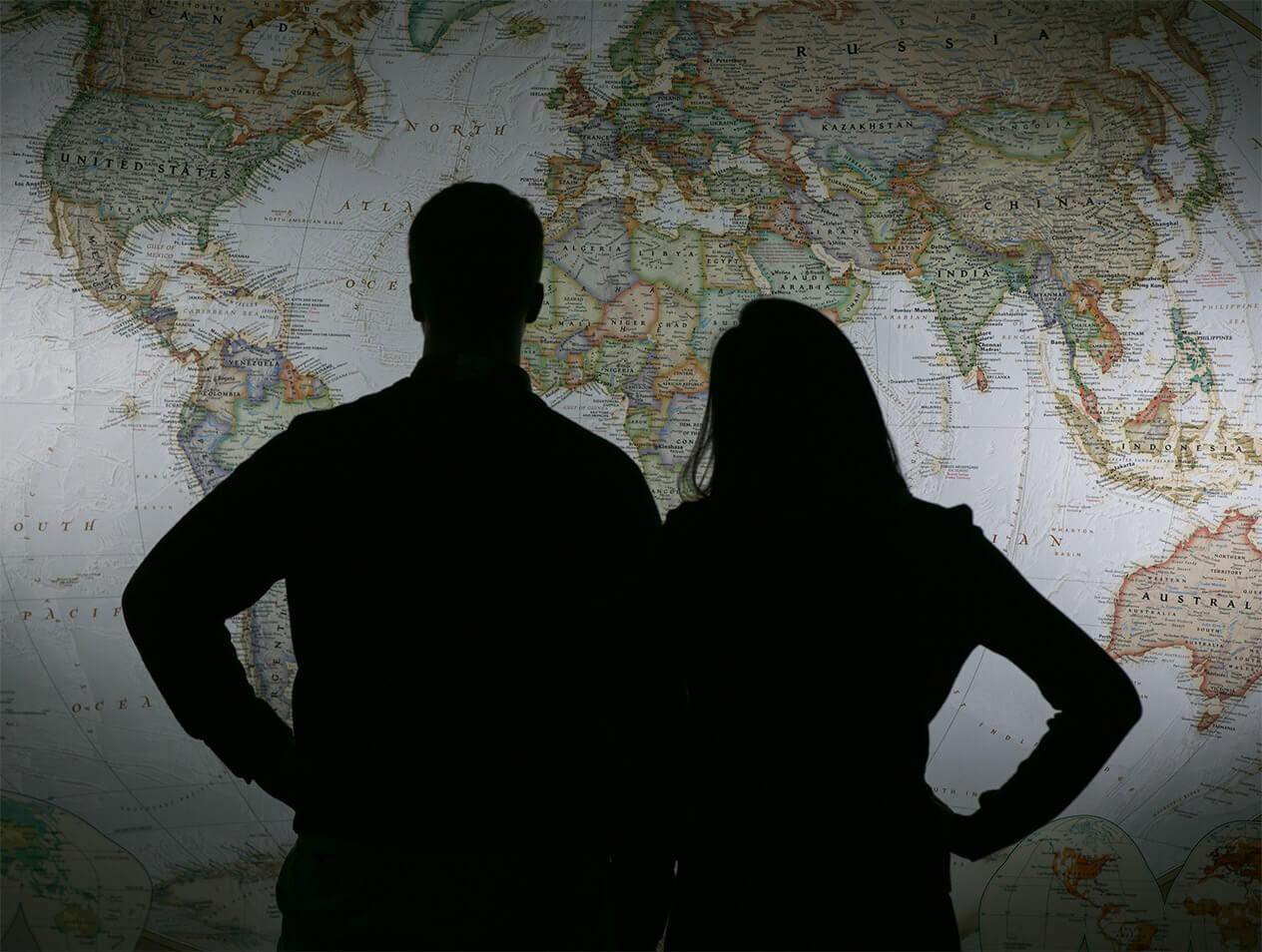 A man and a woman silhouetted in front of a world map