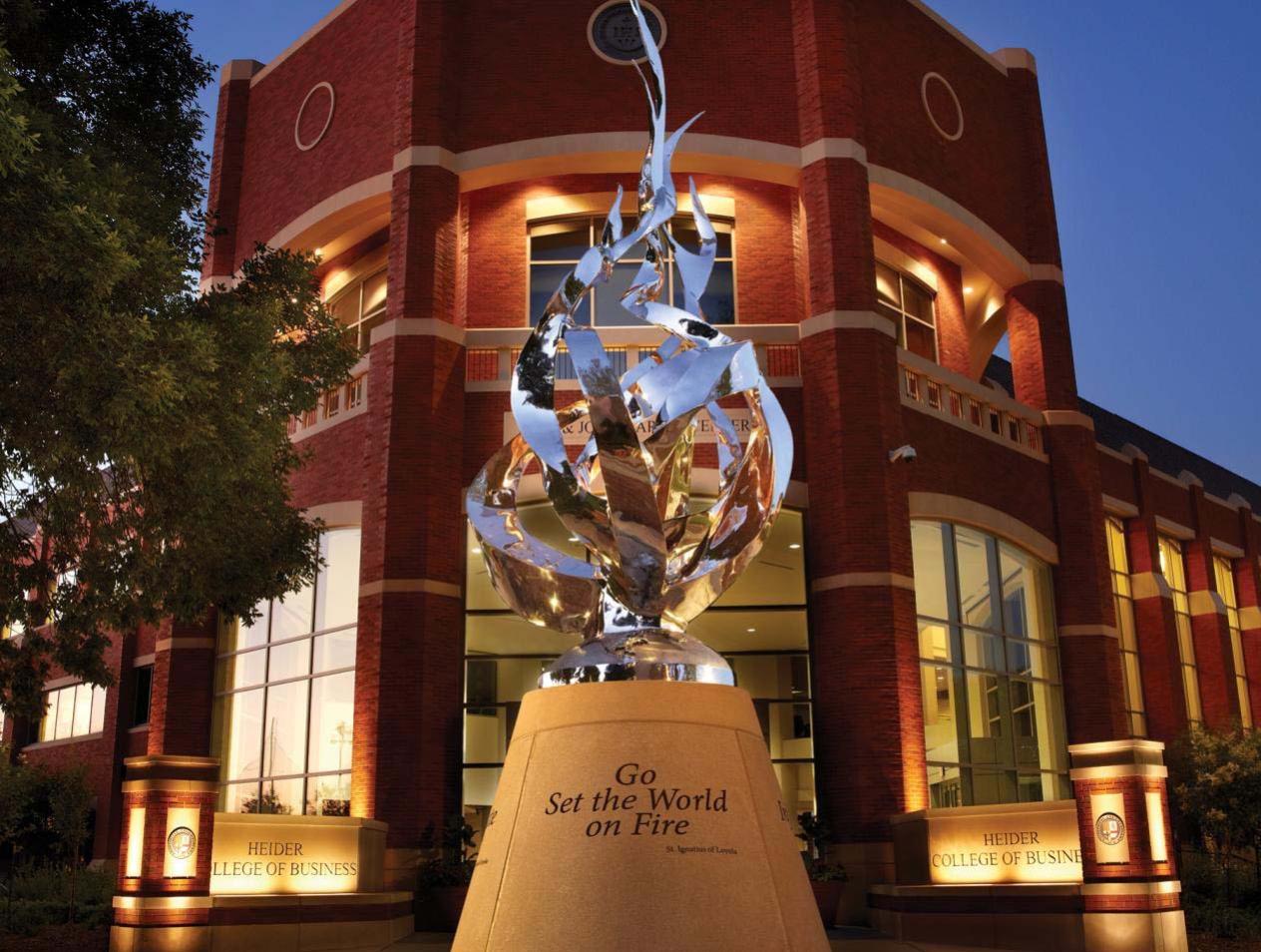 Evening view of flame sculpture outside of Heider Business College displaying the message Go Set the World on Fire.
