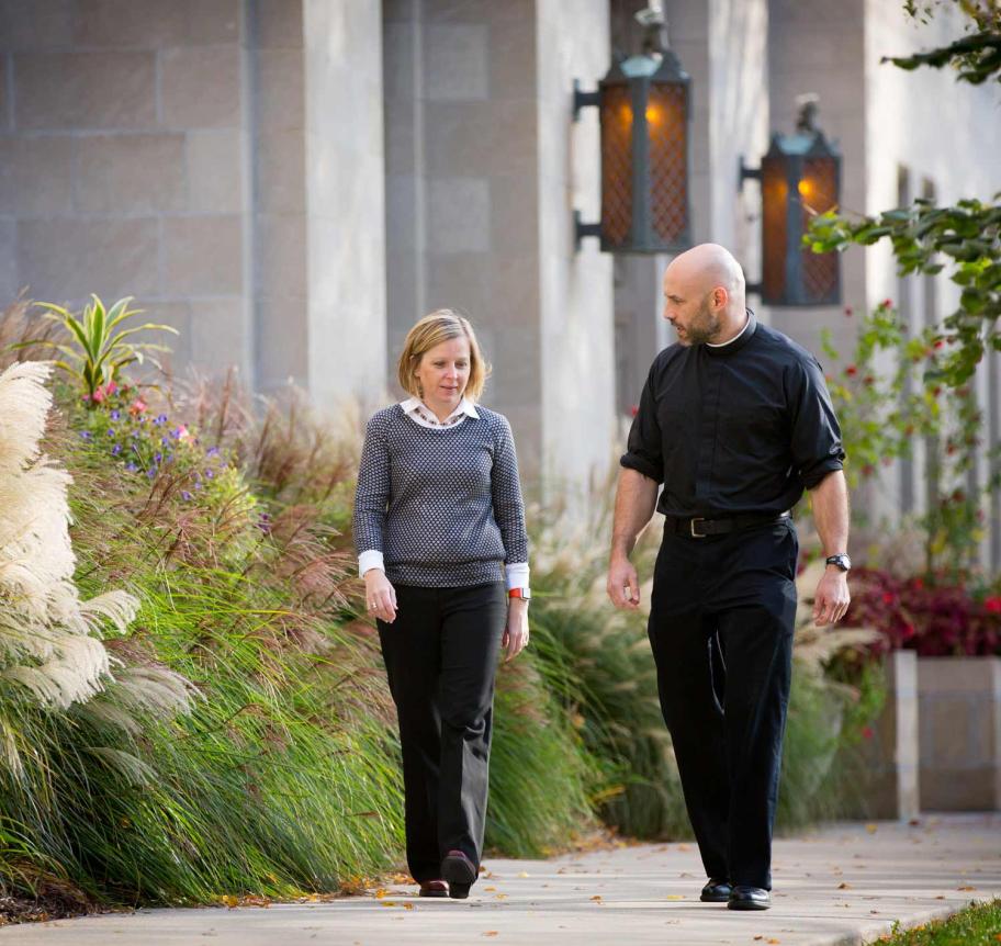 Jesuit faculty walking on campus with colleague