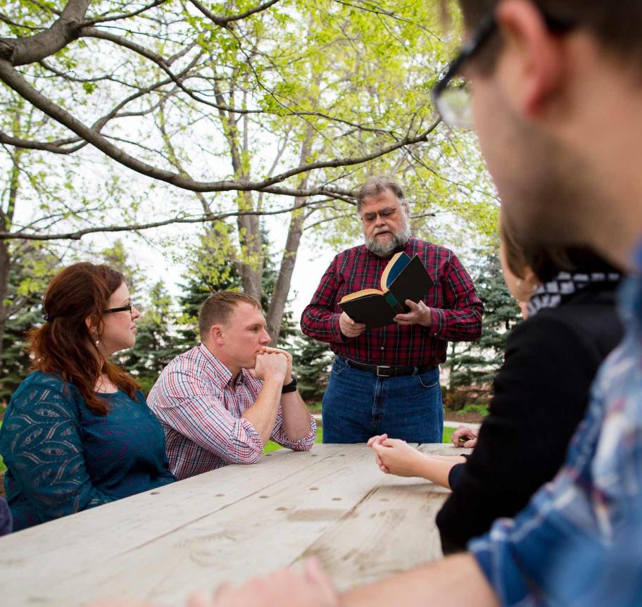 Faculty in book discussion with students in outdoor setting