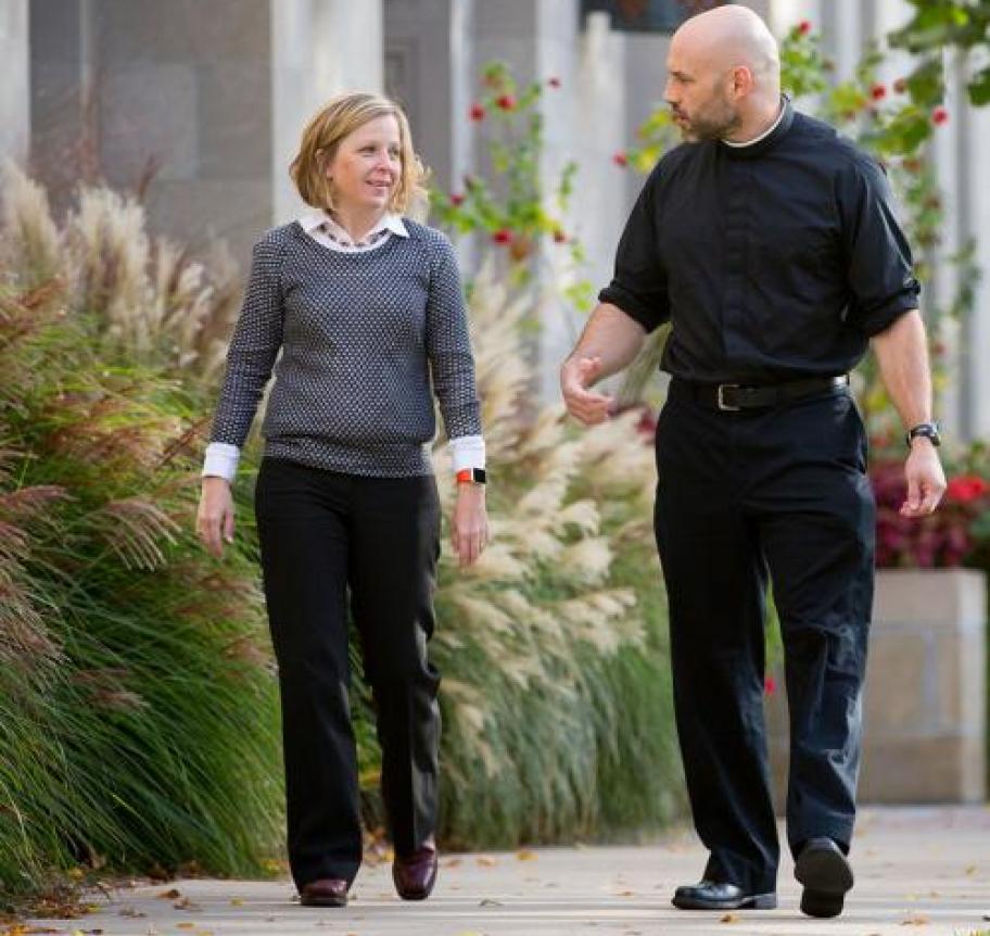 A priest and a woman speaking together while walking
