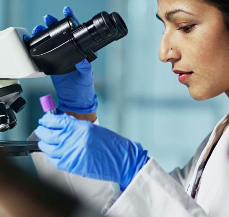 A female scientist checks a lab sample with a microscope