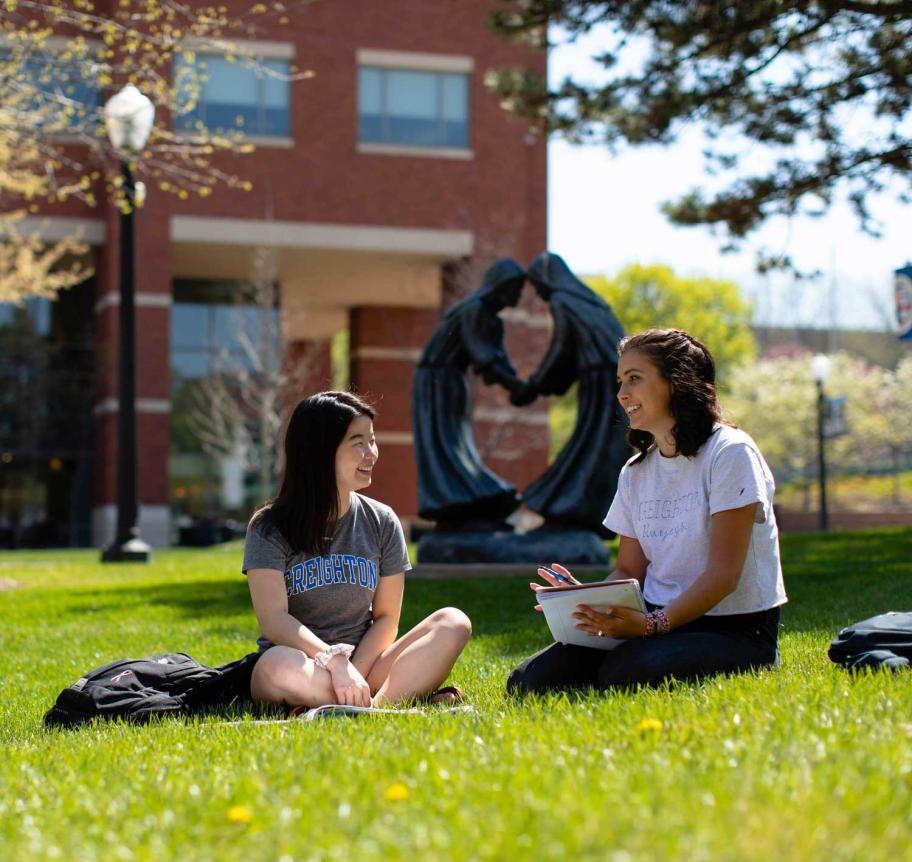 Two students sitting in grass on Creighton campus