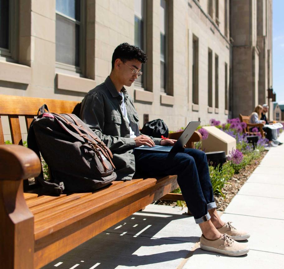 Student on bench outdoors by Creighton Hall