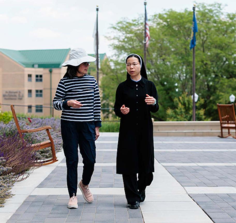 Nun and student talking and walking on campus.