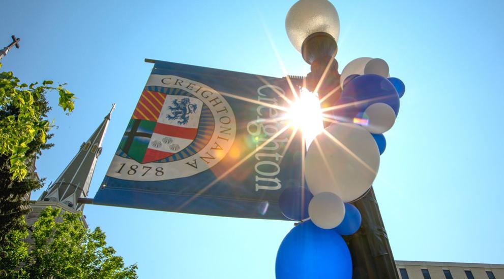 Sun burst coming through Creighton flag on pole ordained with blue and white blues.