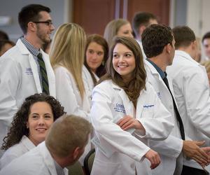 Students in white coats smiling at event