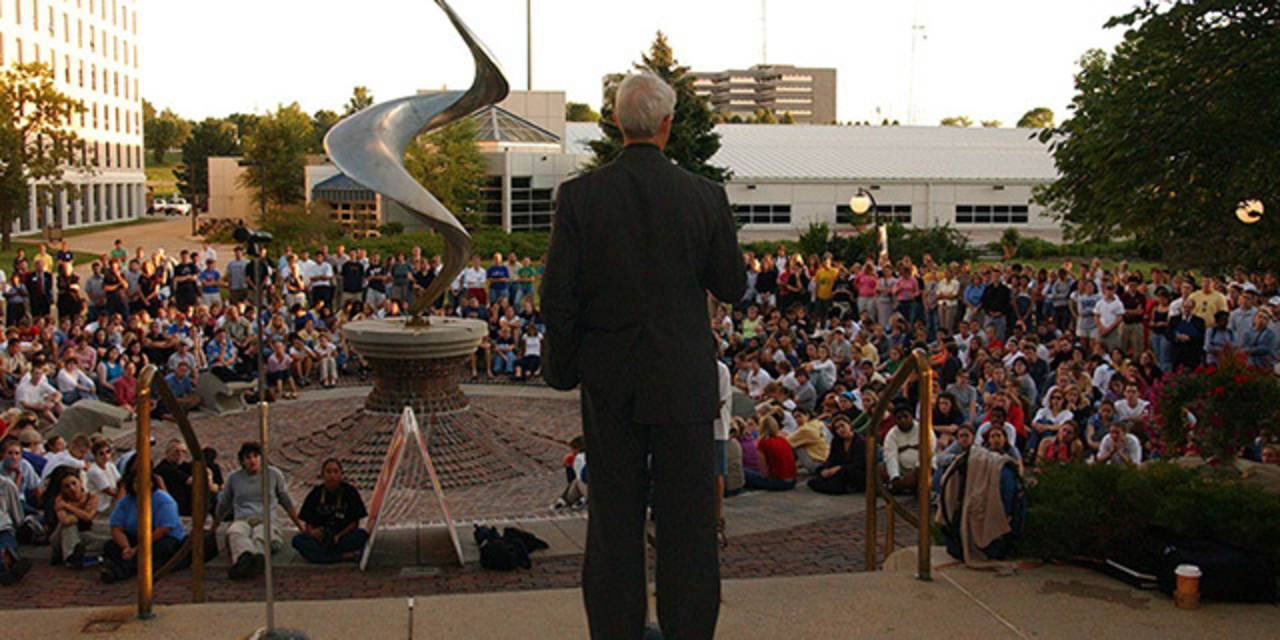 Father Hendrickson speaking to students around flame sculpture.