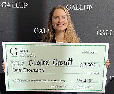 Claire Orcutt holding $1,000 large check from winning Gallup competition.