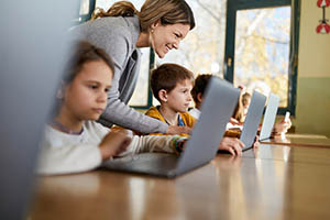 Teacher working with young students on laptops.