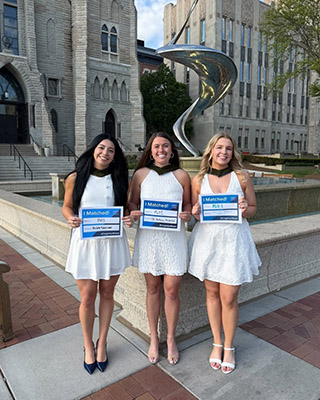 Students pose near flame fountain statue on campus.
