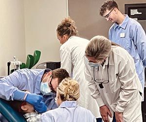 A team of dental professionals in masks and lab coats gather around a child in a dental chair, providing collaborative care.