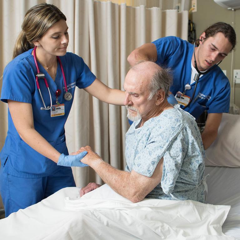Two medical professionals assist a patient in a hospital bed