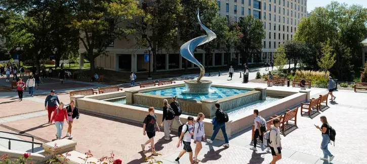 Students walking near flame fountain on mall.