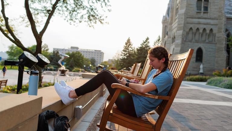 Undergraduate student sitting in rocking chair in front of Creighton Hall