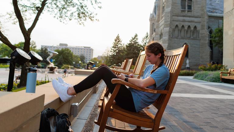 Student studying outside on campus outside St. John's church in oversized rocking chair.
