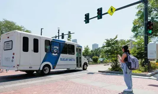 Student on sidewalk as shuttle arrives.