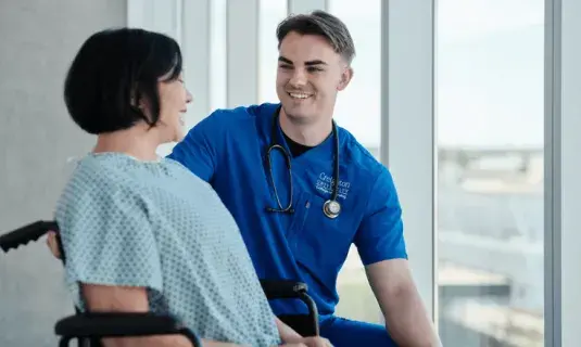 Nursing student kneeling and talking to patient. 