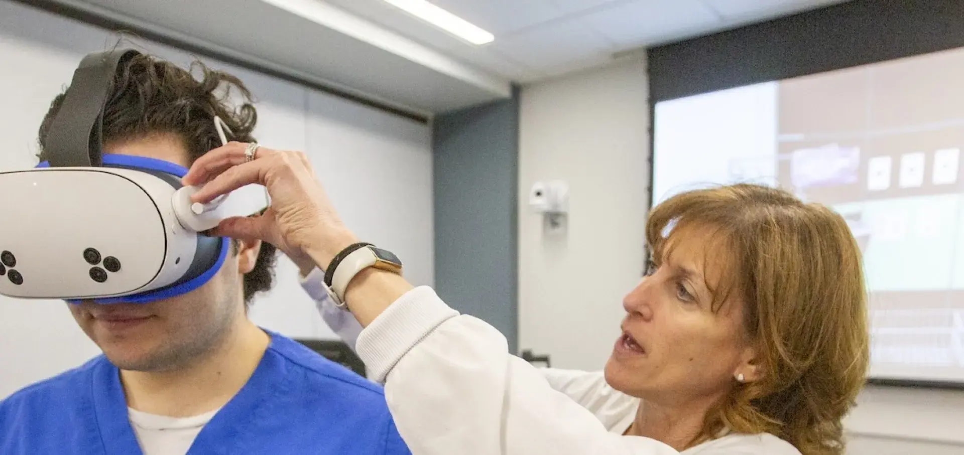 Professor adjusting VR goggles for student.