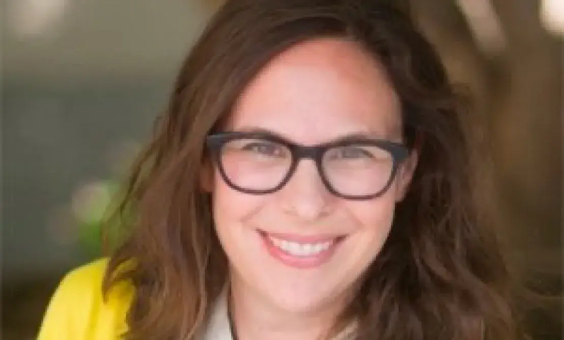 Headshot of Sharrona Pearl, with brown shoulder length hair and glasses, a yellow sweater over a blue and white outfit with white collar