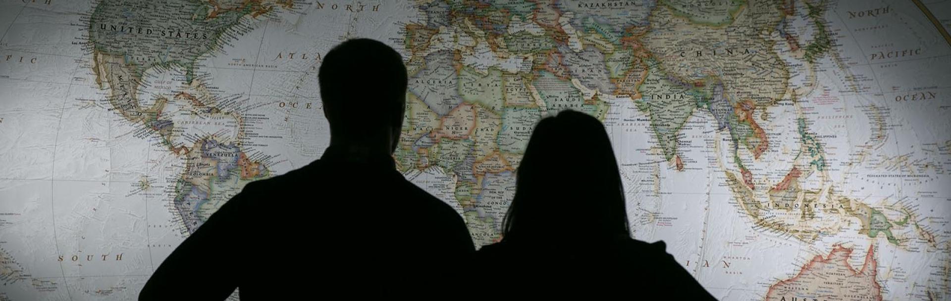 Woman and man silhouetted in front of world map