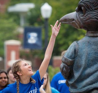 Student touching Billy Bluejay statue beak.