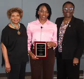 Three women pose with a plaque recognizing the 2024 Annual Dr. Jeffrey M. Smith Memorial Lecture.