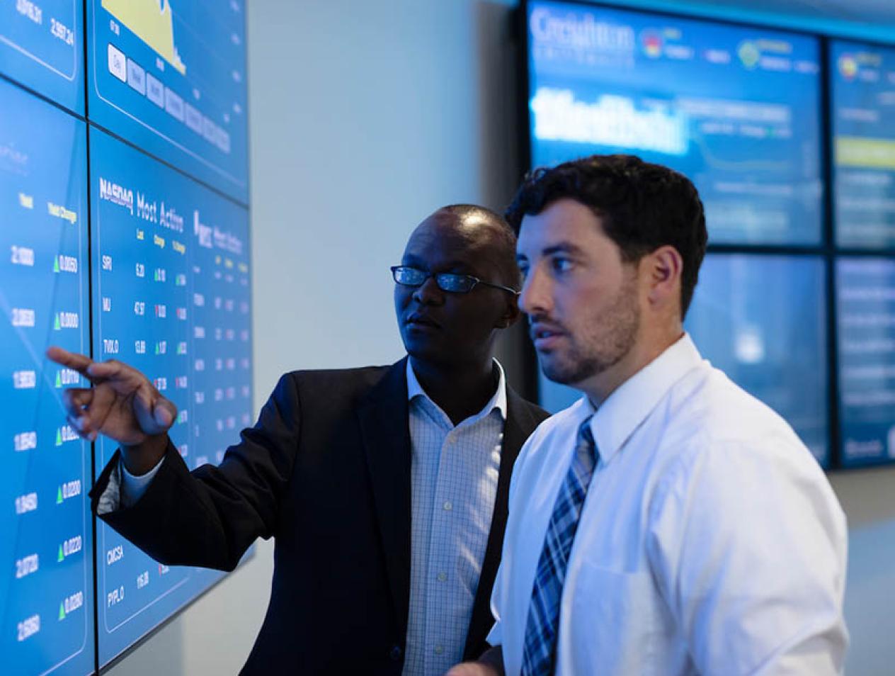 Two academics studying financial data on large classroom displays.