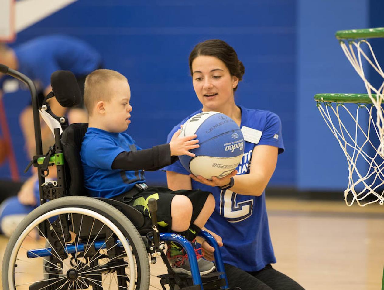Instructor helping disabled child with basketball.