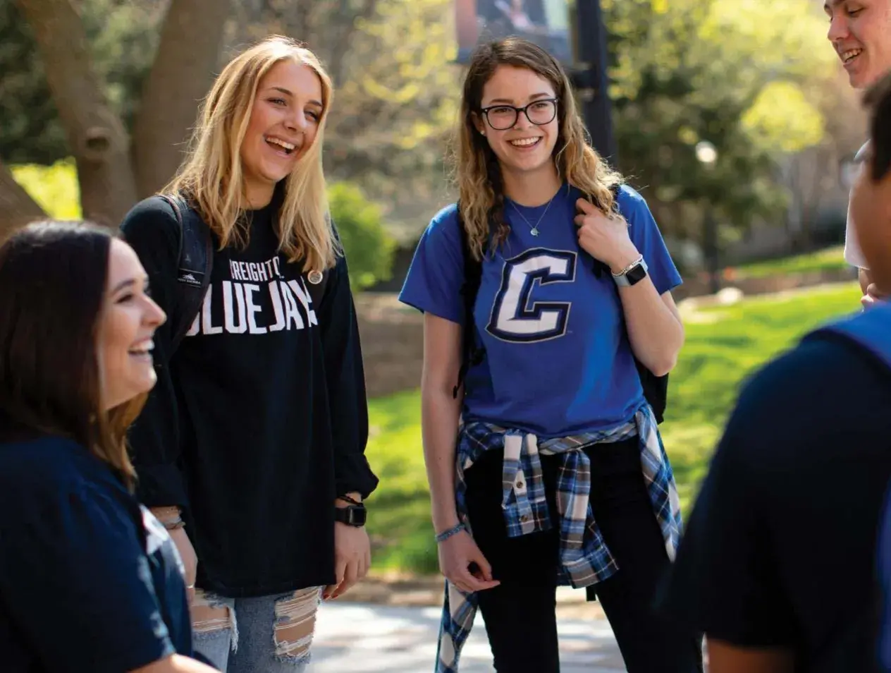 Students gathered in a small group talking and laughing in campus exterior scene.