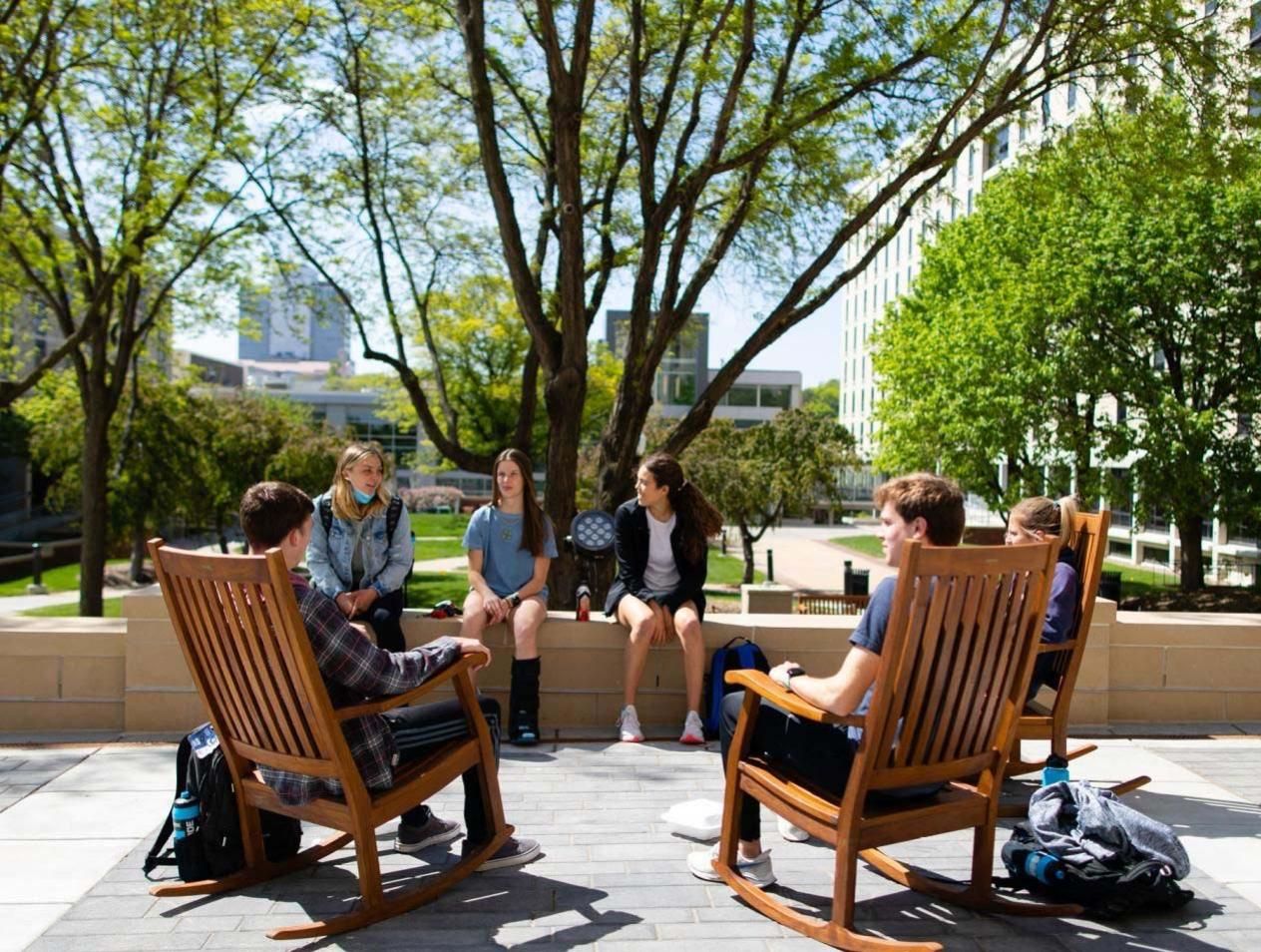 Students sitting on campus outside in oversized rocking chairs.