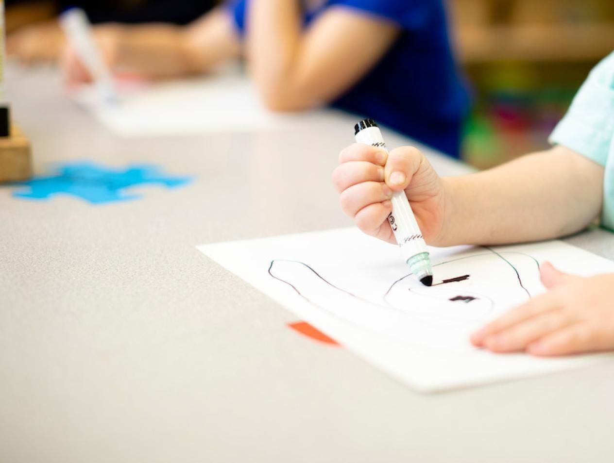 Child using markers in classroom setting.