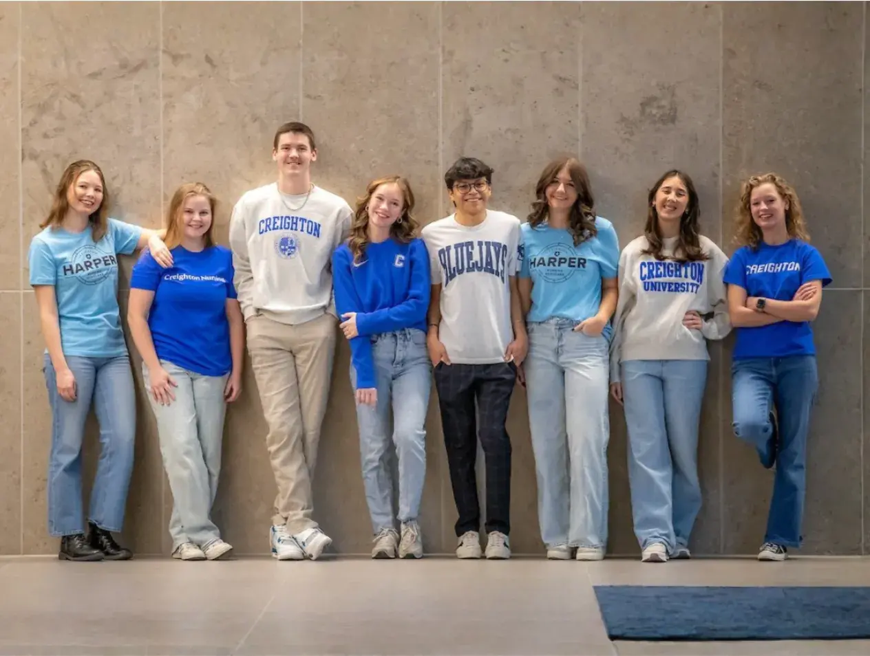 Eight students lined up in front of a wall.