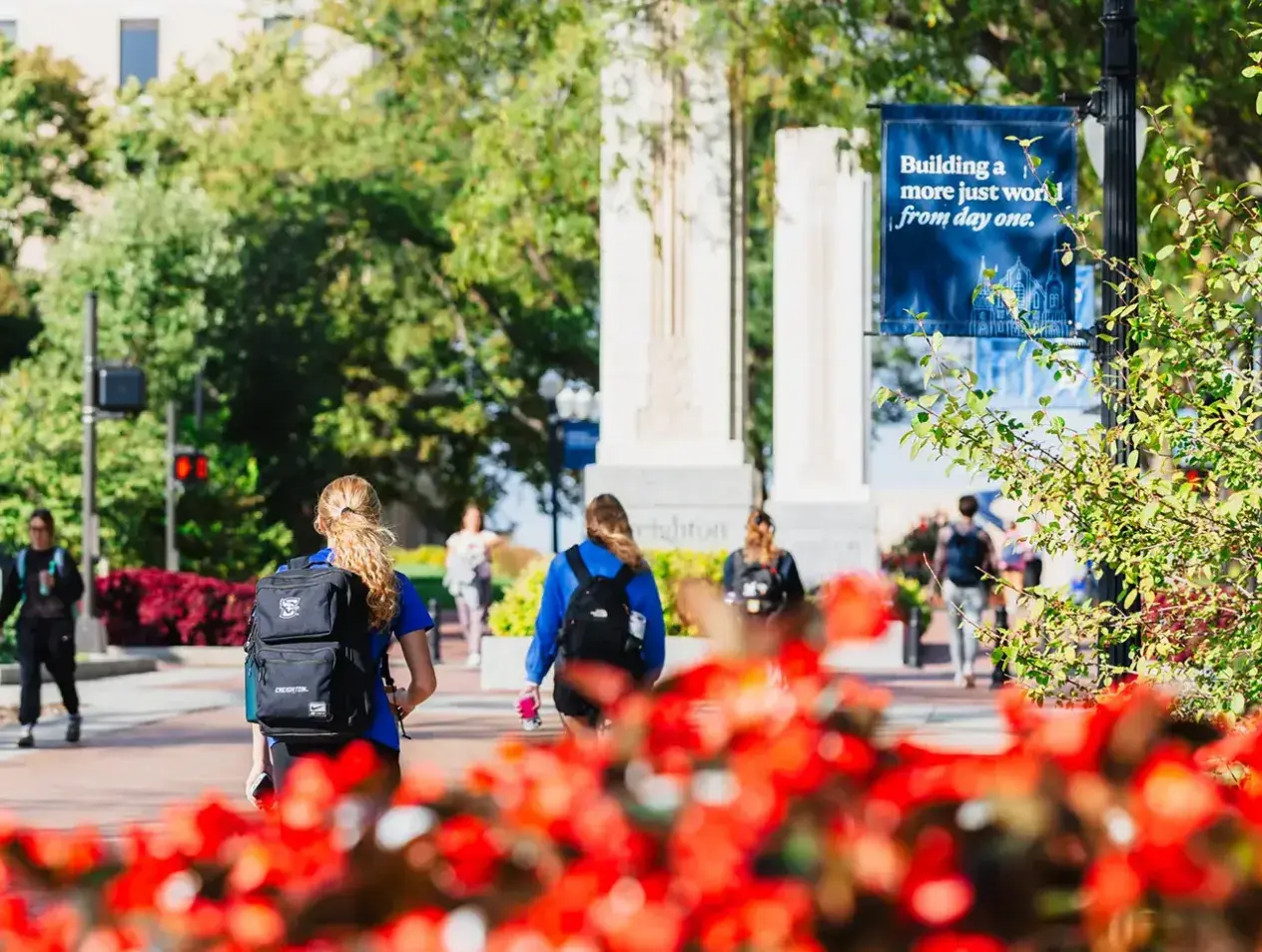 Students walking on Creighton mall with red flowers in foreground.