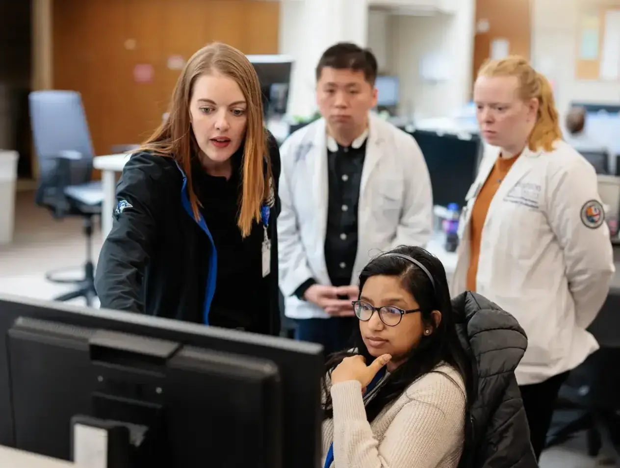 Staff members in white coats gathered with student at computer station.
