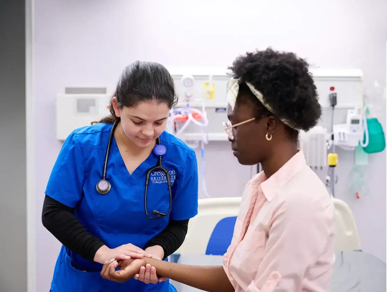Female nursing student examining female patient's wrist