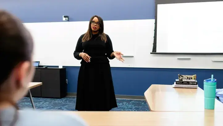 Woman in front of classroom setting.