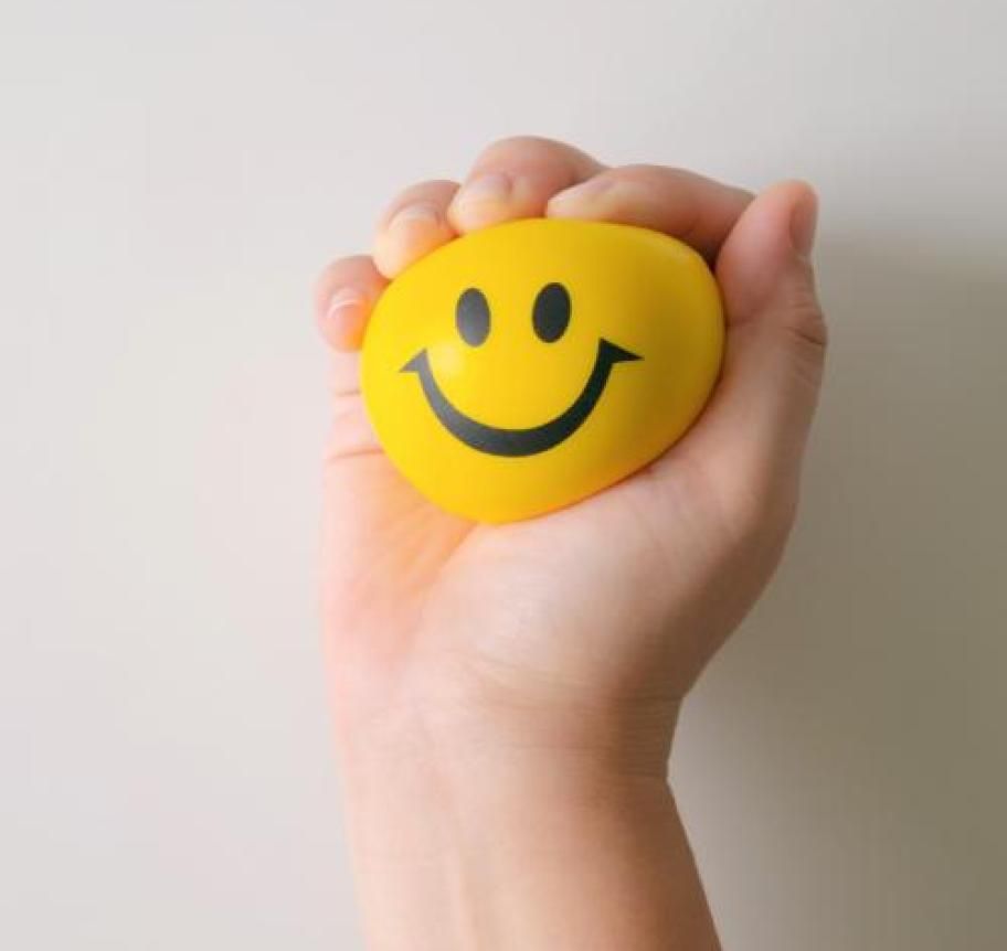 A hand gripping a yellow smiley face stress ball Thumbnail