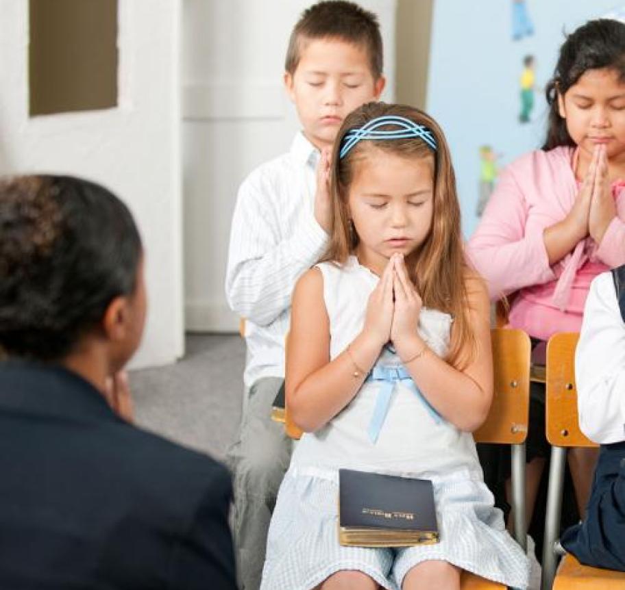 A Catholic teacher praying with young students