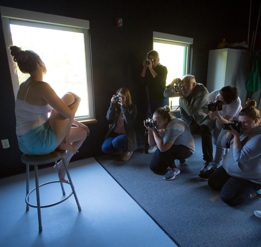 Students photographing a model on a stool in studio