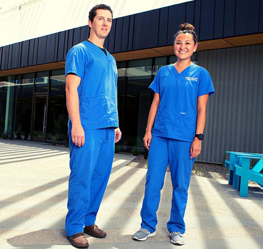 Two health care students standing in blue uniforms.