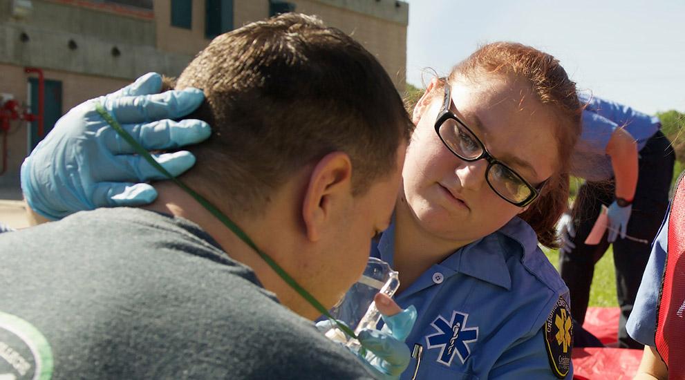 A female EMS student assists a man with an oxygen mask