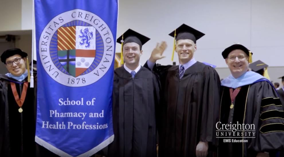 Video thumbnail featuring EMS degree graduates standing by the School of Pharmacy & Health Professions banner