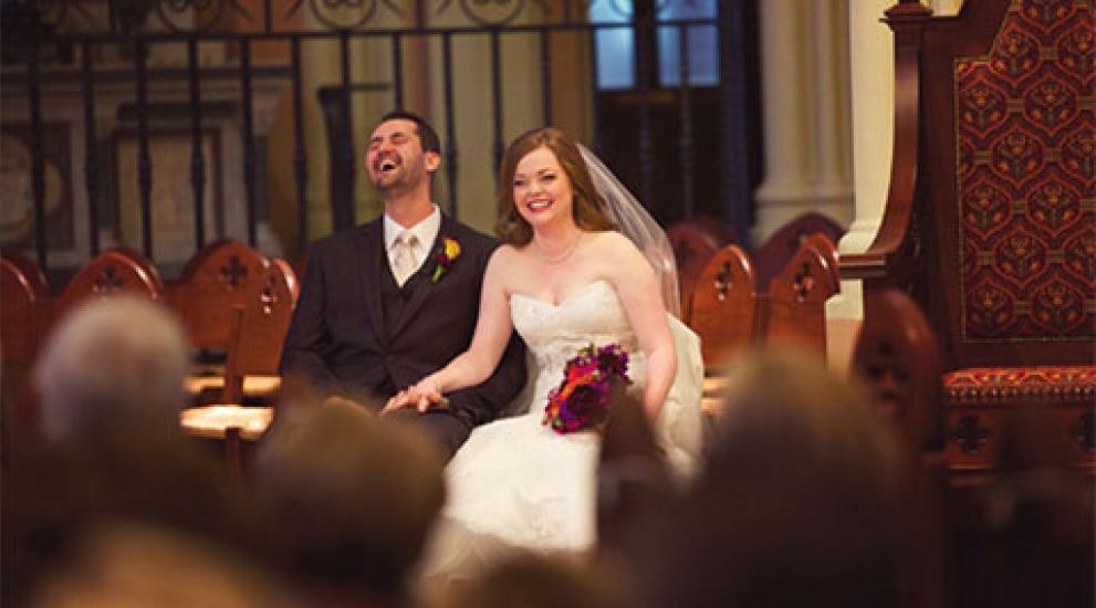 A bride and groom sitting in a pew and laughing during their wedding
