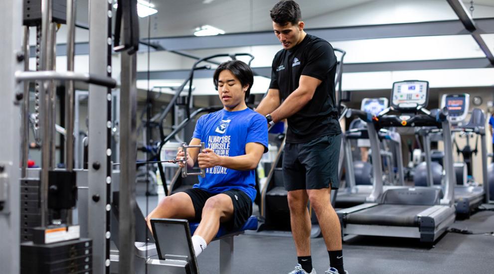 Student exercising in the gym with a personal trainer.